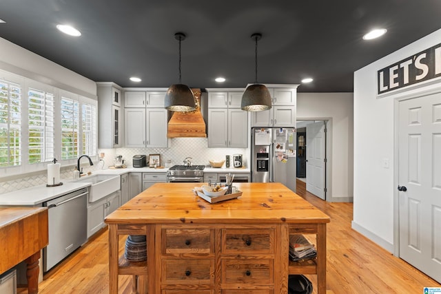 kitchen featuring light hardwood / wood-style flooring, hanging light fixtures, sink, custom exhaust hood, and appliances with stainless steel finishes