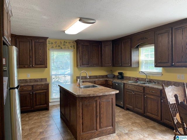 kitchen with a textured ceiling, appliances with stainless steel finishes, sink, and a center island with sink