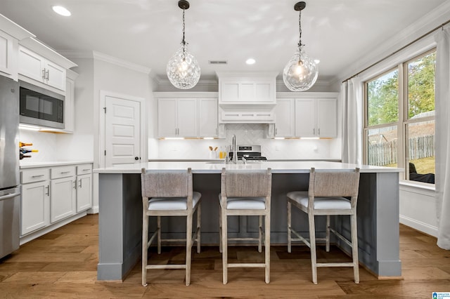 kitchen featuring appliances with stainless steel finishes, light hardwood / wood-style flooring, a kitchen island with sink, and pendant lighting