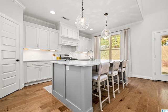 kitchen featuring stainless steel stove, a center island with sink, decorative light fixtures, white cabinets, and light hardwood / wood-style floors