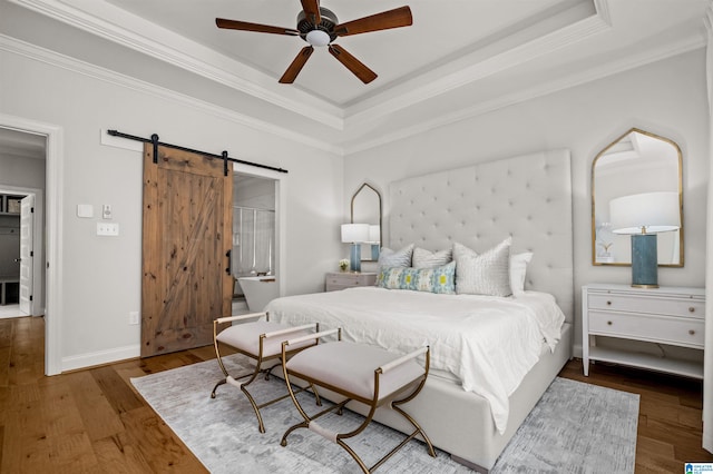 bedroom with a barn door, a tray ceiling, dark hardwood / wood-style flooring, ceiling fan, and ornamental molding