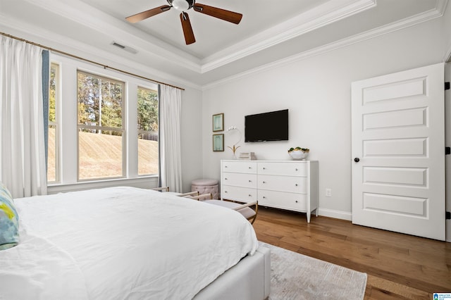 bedroom with ceiling fan, a raised ceiling, wood-type flooring, and ornamental molding