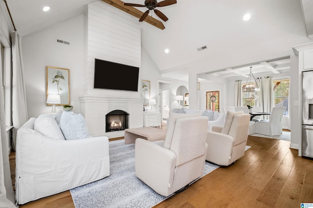 living room with ceiling fan with notable chandelier, a brick fireplace, hardwood / wood-style floors, beam ceiling, and high vaulted ceiling