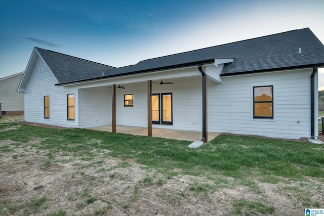 back of property with a shingled roof, a ceiling fan, a yard, and a patio