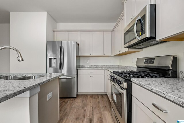 kitchen featuring sink, light stone counters, light wood-type flooring, appliances with stainless steel finishes, and white cabinets