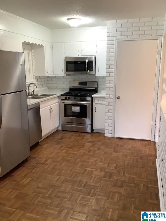 kitchen with appliances with stainless steel finishes, sink, dark parquet flooring, and white cabinets