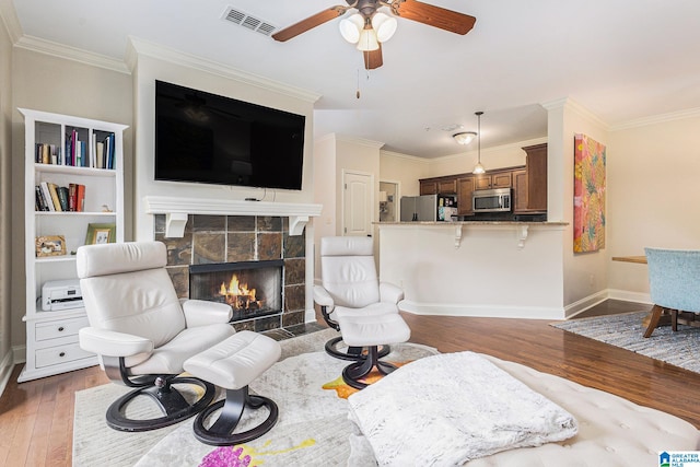 living room with crown molding, dark hardwood / wood-style floors, a tile fireplace, and ceiling fan