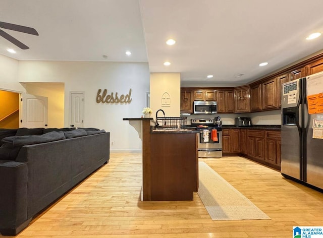 kitchen featuring sink, light hardwood / wood-style floors, stainless steel appliances, ceiling fan, and a breakfast bar area