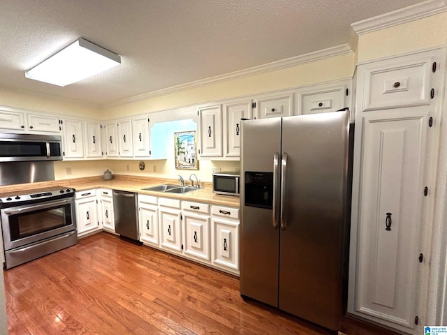 kitchen featuring sink, crown molding, white cabinets, appliances with stainless steel finishes, and light hardwood / wood-style floors