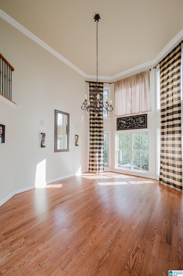 unfurnished dining area featuring a high ceiling, hardwood / wood-style flooring, ornamental molding, and a notable chandelier