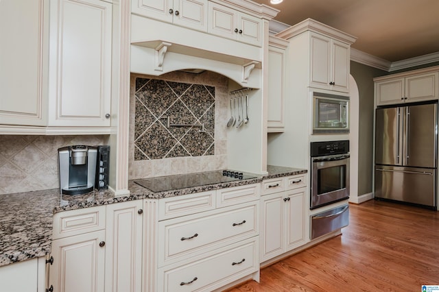 kitchen with crown molding, dark stone counters, backsplash, appliances with stainless steel finishes, and light hardwood / wood-style flooring