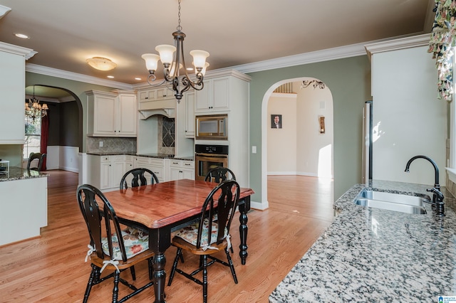 dining space with sink, a notable chandelier, light hardwood / wood-style floors, and crown molding