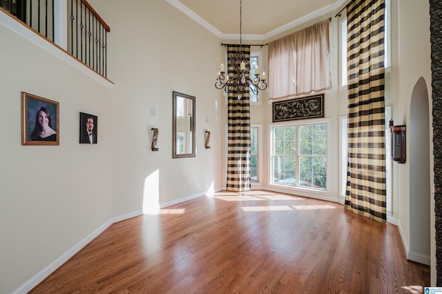 unfurnished dining area featuring hardwood / wood-style flooring, a high ceiling, an inviting chandelier, and crown molding