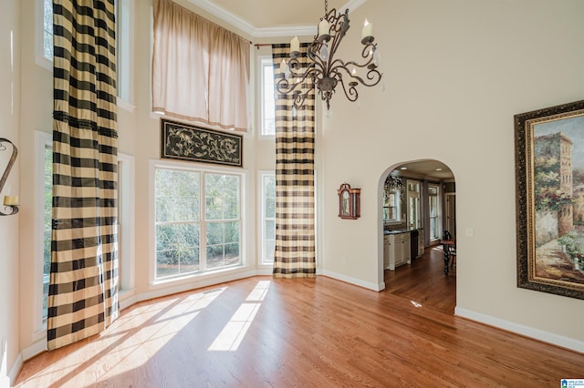 unfurnished living room featuring a towering ceiling, a chandelier, light hardwood / wood-style flooring, and crown molding