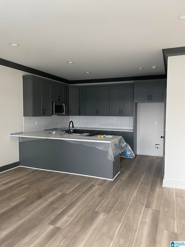 kitchen featuring kitchen peninsula, hardwood / wood-style floors, tasteful backsplash, and sink