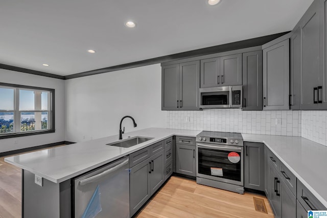 kitchen featuring a peninsula, stainless steel appliances, a sink, and gray cabinetry