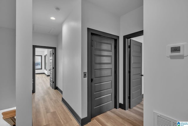 corridor with light wood-type flooring, baseboards, visible vents, and attic access