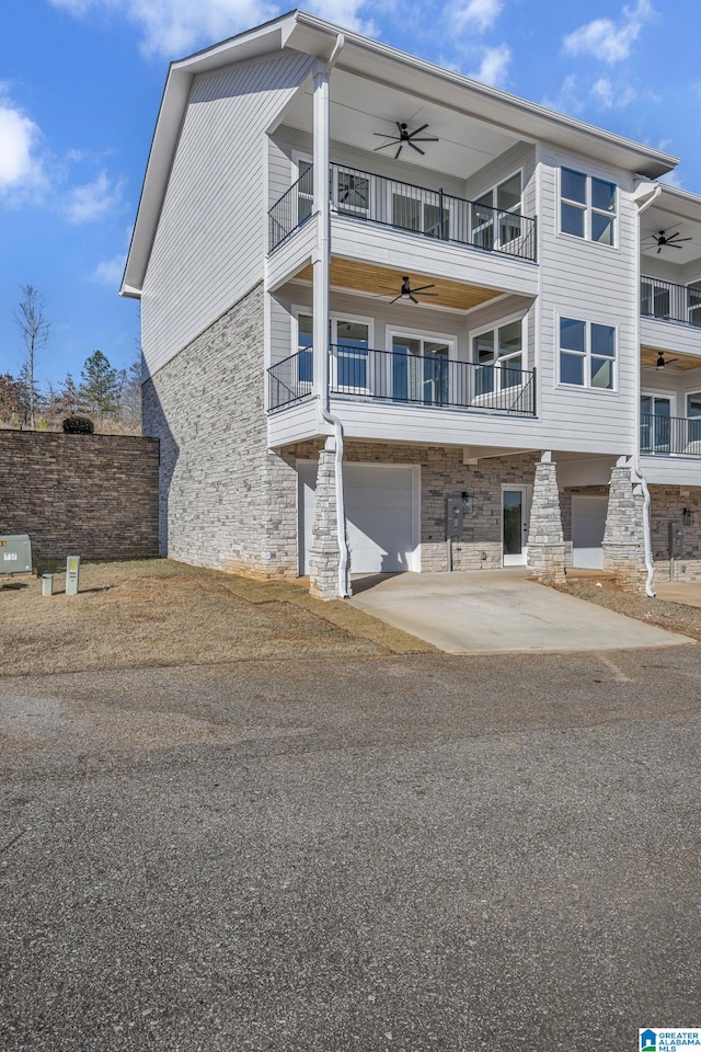 exterior space with a balcony, driveway, ceiling fan, and stone siding