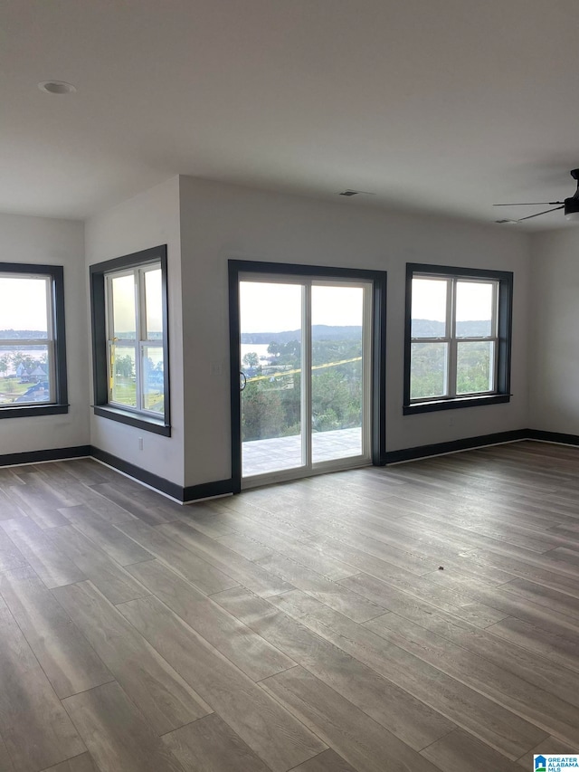 unfurnished room with a wealth of natural light, wood-type flooring, and ceiling fan