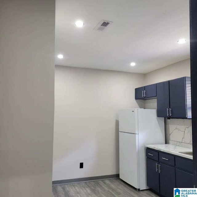 kitchen with tasteful backsplash, light stone countertops, light hardwood / wood-style floors, blue cabinets, and white refrigerator