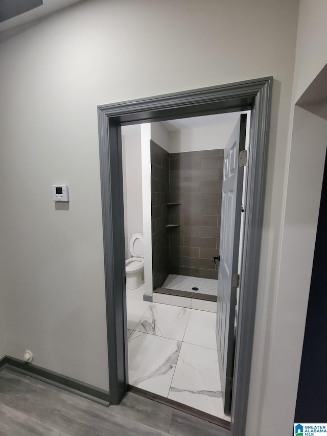 bathroom featuring tiled shower, hardwood / wood-style floors, and toilet