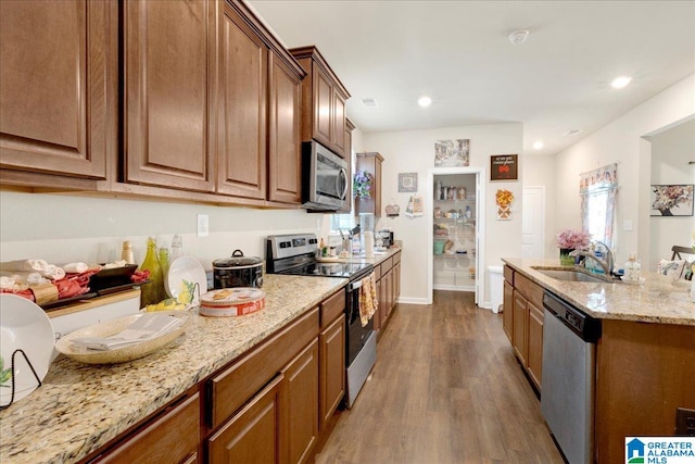 kitchen with hardwood / wood-style flooring, sink, light stone countertops, and stainless steel appliances