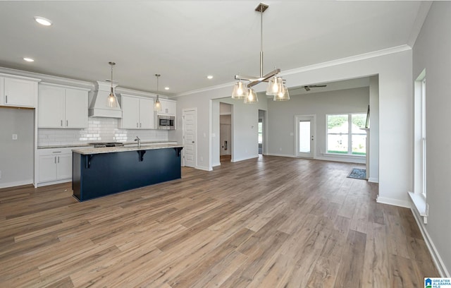 kitchen with decorative light fixtures, white cabinets, a center island with sink, and custom range hood