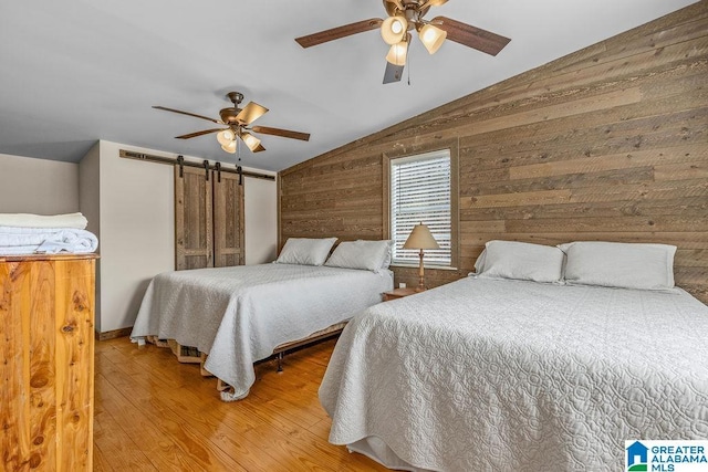 bedroom with ceiling fan, vaulted ceiling, wood walls, and wood finished floors