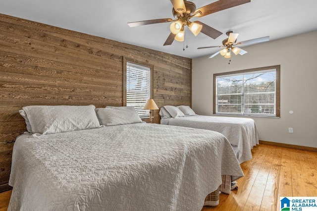bedroom with a ceiling fan, wood walls, light wood-style flooring, and baseboards