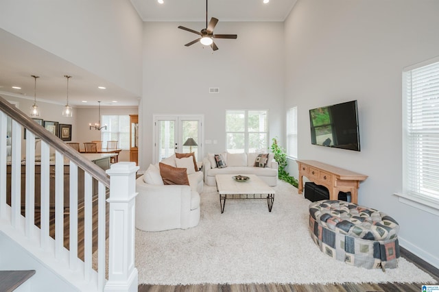 living room with a high ceiling, ceiling fan with notable chandelier, hardwood / wood-style flooring, and a healthy amount of sunlight