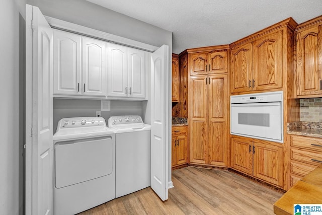 laundry room with cabinets, washing machine and clothes dryer, light hardwood / wood-style flooring, and a textured ceiling