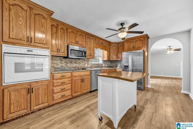 kitchen featuring appliances with stainless steel finishes, light wood-type flooring, backsplash, and ceiling fan