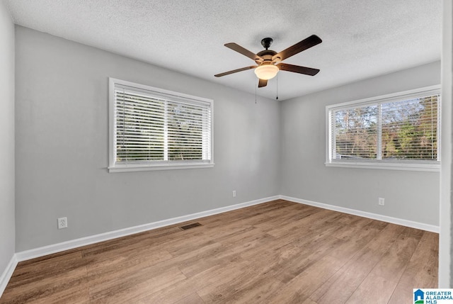 spare room with a textured ceiling, a wealth of natural light, light hardwood / wood-style floors, and ceiling fan