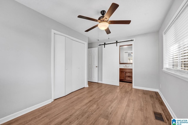 unfurnished bedroom featuring a closet, a barn door, ceiling fan, and light wood-type flooring