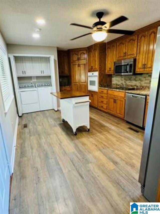 kitchen with stainless steel appliances, tasteful backsplash, washer and clothes dryer, and light wood-type flooring