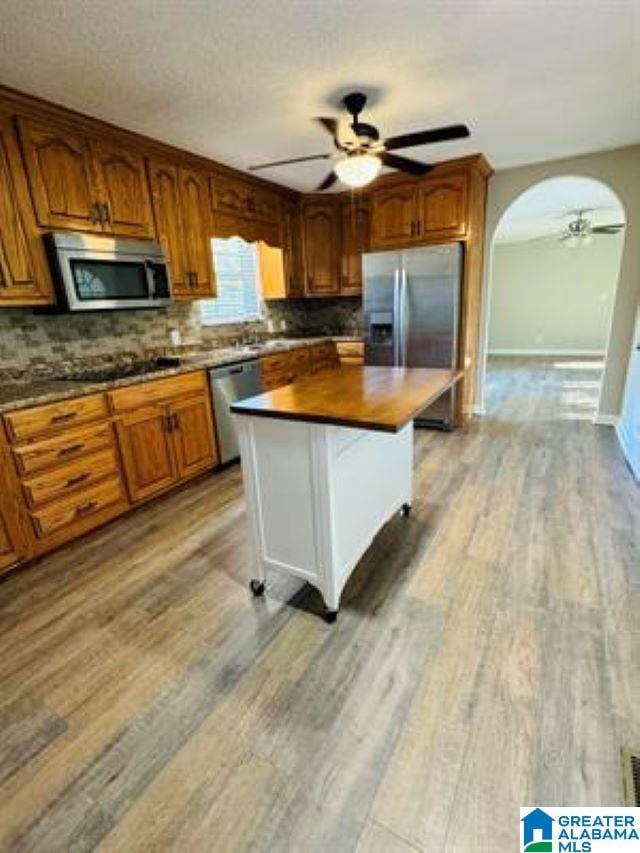 kitchen with a kitchen island, a kitchen breakfast bar, stainless steel appliances, backsplash, and light wood-type flooring