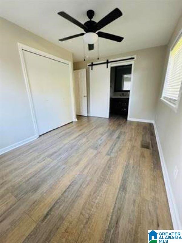 unfurnished bedroom with a closet, hardwood / wood-style floors, a barn door, and ceiling fan