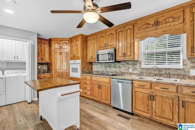 kitchen with appliances with stainless steel finishes, sink, independent washer and dryer, and light hardwood / wood-style floors