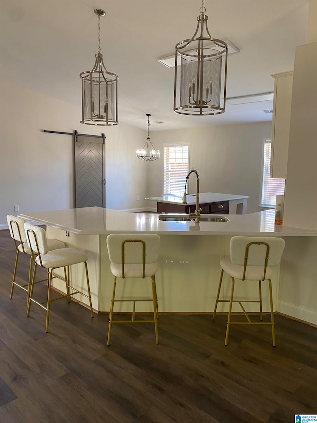 kitchen with sink, a barn door, dark hardwood / wood-style flooring, a kitchen breakfast bar, and decorative light fixtures