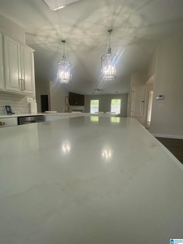 interior space with backsplash, white cabinetry, stainless steel dishwasher, ceiling fan with notable chandelier, and decorative light fixtures