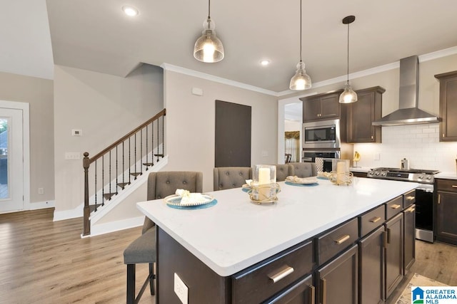 kitchen with wall chimney exhaust hood, a center island, stainless steel appliances, and light hardwood / wood-style floors