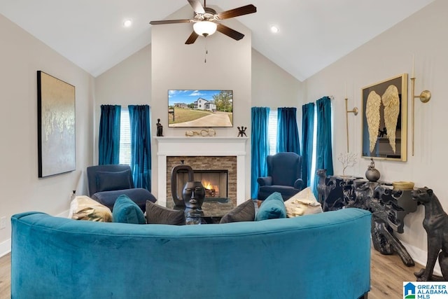 living room featuring light hardwood / wood-style flooring, a stone fireplace, high vaulted ceiling, and ceiling fan