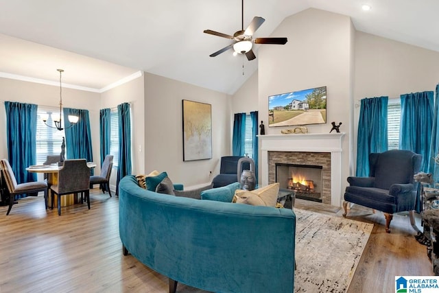 living room featuring light wood-type flooring, ceiling fan with notable chandelier, a fireplace, crown molding, and high vaulted ceiling