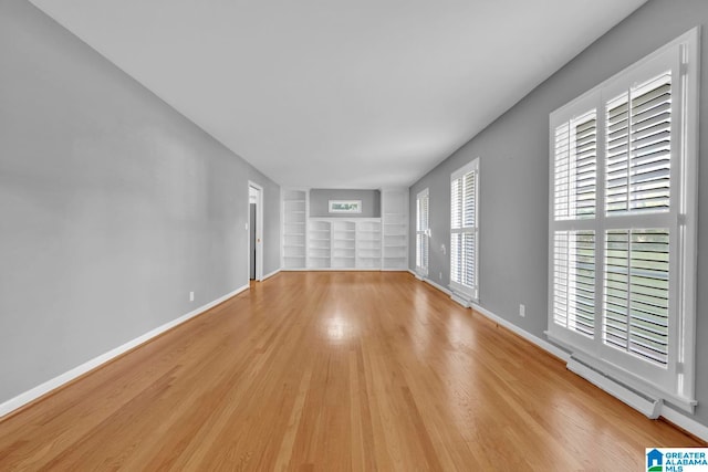 unfurnished living room featuring light wood-type flooring, a wealth of natural light, and a baseboard radiator