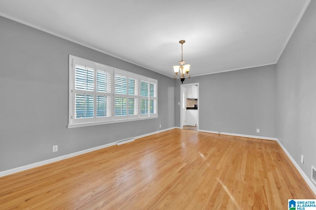 spare room featuring light wood-type flooring, a notable chandelier, and crown molding