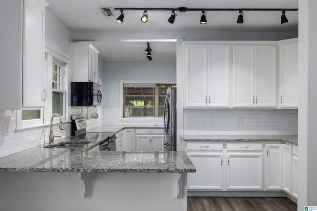 kitchen with white cabinets, kitchen peninsula, tasteful backsplash, light stone countertops, and appliances with stainless steel finishes