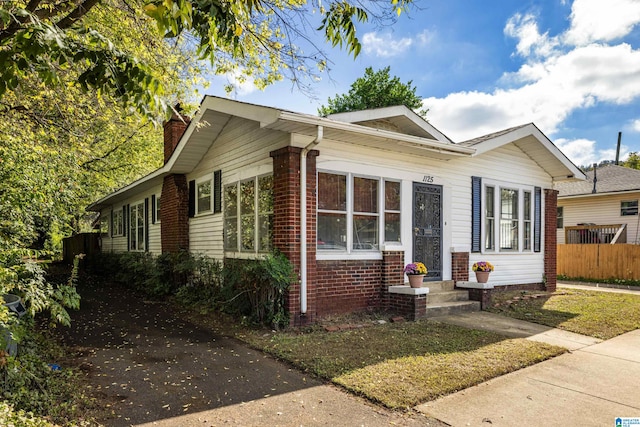 bungalow with brick siding, a chimney, and fence