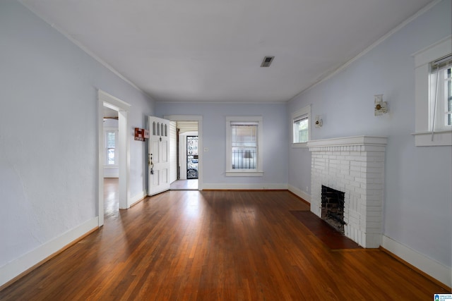 unfurnished living room featuring dark wood-type flooring, ornamental molding, and a brick fireplace