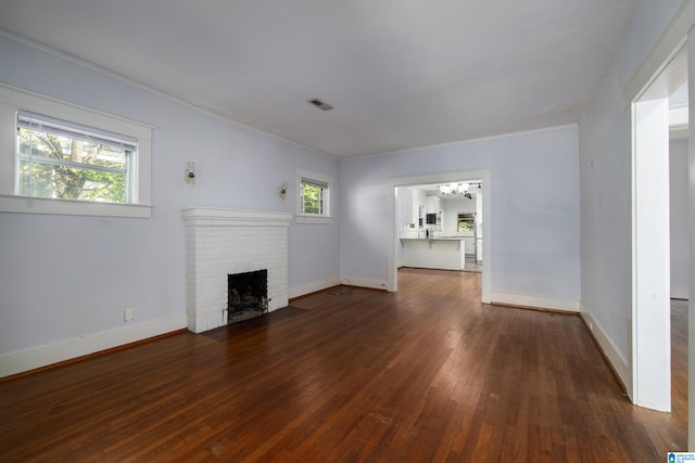 unfurnished living room featuring dark hardwood / wood-style flooring, ornamental molding, a healthy amount of sunlight, and a fireplace