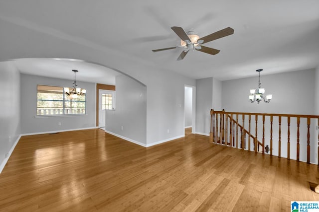 empty room with wood-type flooring and ceiling fan with notable chandelier